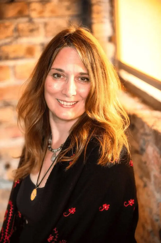 Smiling woman with light brown hair in a cozy setting.